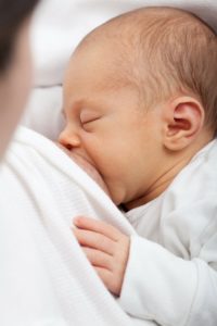 A relaxed newborn baby breastfeeding, looking sleepy and content. Baby's hand is resting on mother's breast.