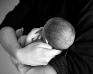 Black and white image of a newborn baby held in parent's arms.