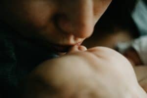 A soft focus image of a mother kissing the face of her sleeping newborn